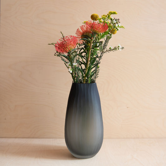Dark gray vase with flowers on a wooden surface and beige background