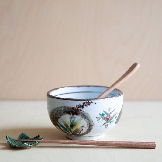 Ceramic bowl with floral design, wooden spoon, and chopsticks on a beige background