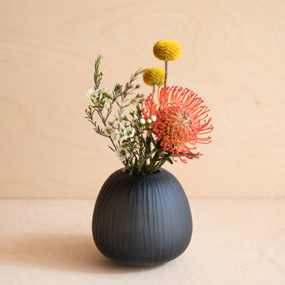 Black ribbed vase with colorful flowers on a beige background