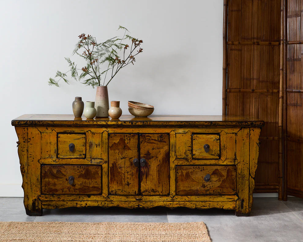 Vintage wooden sideboard with decorative items against a white wall.