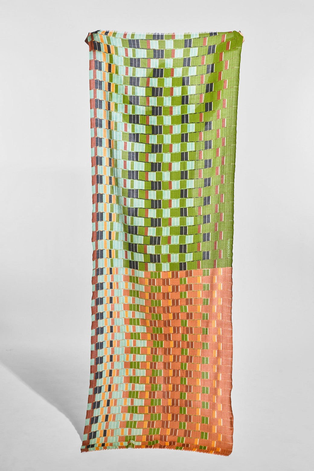 A wool scarf with a multicolor geometric pattern, featuring a green and orange checkerboard design, hanging against a light gray background.