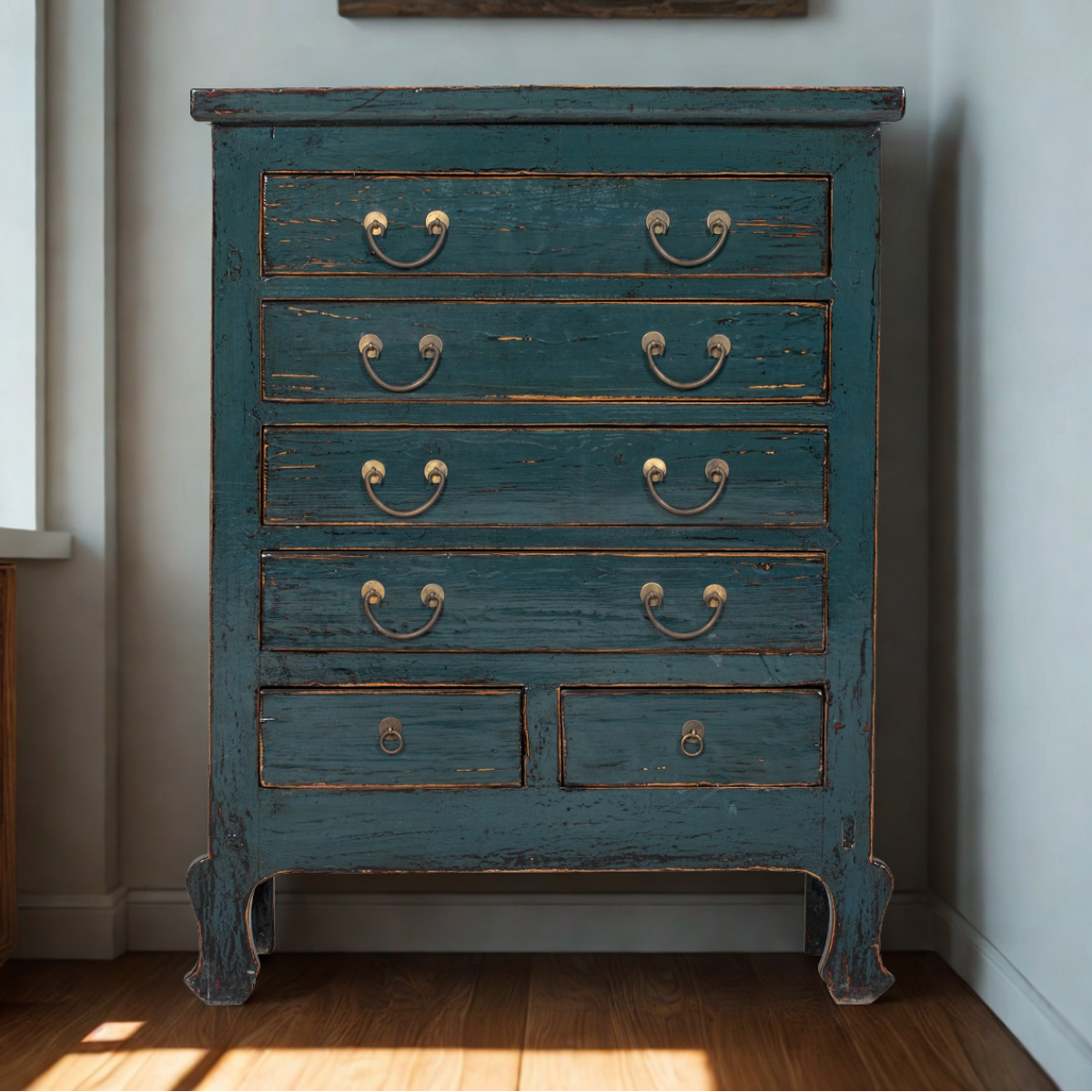 Vintage blue dresser with chipped paint in a room with a window and light-colored walls.