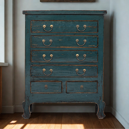 Vintage blue dresser with chipped paint in a room with a window and light-colored walls.