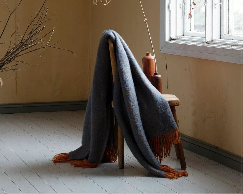 Blue blanket draped over a wooden chair in a room with a window and decorative elements.